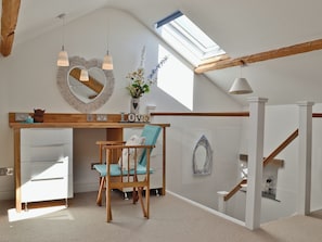 Ein Loft-Zimmer mit schrägem Dach, einem Oberlicht, einem Holztisch, einem blauen Stuhl, einer weißen Kommode und einer Treppe.