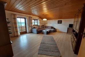 Ein gemütliches Wohnzimmer mit Holzboden, einer Couch, einem Couchtisch und Blick durch ein Fenster.