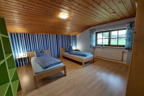 Ein Zimmer mit zwei Holzbetten, einem Fenster mit Vorhängen, einem Heizkörper und einer schrägen Decke.