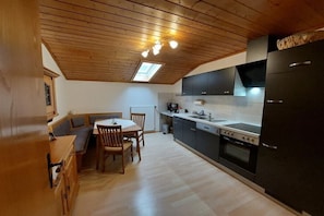 Eine kleine Küche mit Holzbalkendecke, einem Esstisch mit Stühlen, einem schwarzen Kühlschrank und einem Herd.