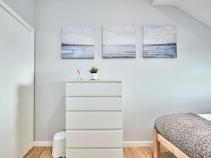 A bedroom with a bed, a white dresser, a small potted plant, and three wall-mounted paintings. - No.6 Golf Terrace Apartments - UK52021 (Portrush)