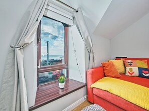 A room with a window, a red sofa, and a small plant on the windowsill. - No.6 Golf Terrace Apartments - UK52021 (Portrush)