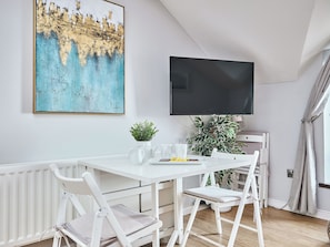 A white dining table with chairs, a flat-screen TV mounted on the wall, and a large abstract painting above the table. - No.6 Golf Terrace Apartments - UK52021 (Portrush)
