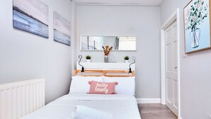 Une chambre à coucher comprenant un lit, une table de chevet avec un miroir, une étagère murale agrémentée d’objets décoratifs et une porte.