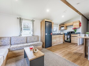 A compact living space with a sofa, a small coffee table, a kitchen area with wooden cabinets and appliances, and a window with curtains. - 3 bedroom accommodation in Bideford (Bideford)