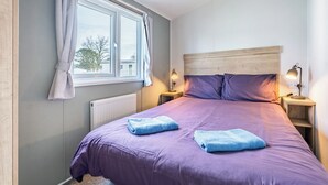 Een slaapkamer met een bed, twee bedlampen, een raam met gordijnen en een radiator.