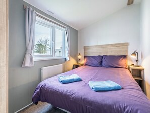 A bedroom with a bed, two bedside lamps, a window with curtains, and a radiator. - 3 bedroom accommodation in Bideford (Bideford)