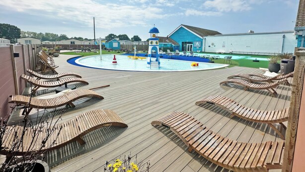 A pool area with lounge chairs, a water play structure, and a building with a blue exterior. - Hayling Island Retreat (Hayling Island)