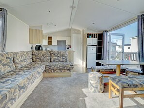 A modern living room with a sectional sofa, a dining table, and a kitchen area visible through an open door. - Hayling Island Retreat (Hayling Island)