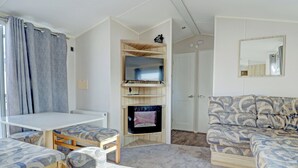 A furnished room with a dining table, two chairs, a sofa, a TV on a wooden stand, a mirror, and a door. - Hayling Island Retreat (Hayling Island)