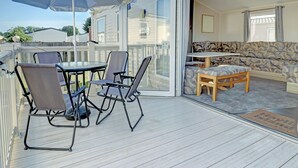 A deck with a table and chairs, a blue umbrella, and a sliding glass door leading to an interior with a sofa and a small table. - Hayling Island Retreat (Hayling Island)