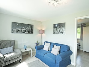 A living room with a striped armchair, a blue sofa, and two black-and-white cityscape paintings on the wall.
