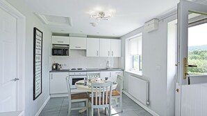 Een moderne keuken met witte kastjes, een eettafel met stoelen, een magnetron en een raam met uitzicht.