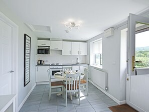 A modern kitchen with white cabinets, a dining table with chairs, a microwave, and a window with a view. - 2 bedroom accommodation in Brecon, Near Hay-on-Wye (Brecon, Near Hay-on Wye)