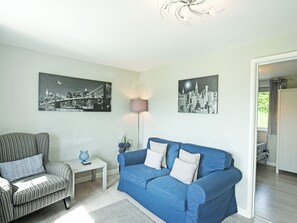 Un salón con un sillón a rayas, un sofá azul y dos cuadros con paisajes urbanos blanco y negro en la pared.