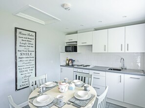 Una cocina moderna con armarios blancos, microondas, lavaplatos y una zona de comedor con platos, tazas y hervidor.