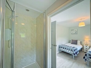 Un dormitorio con cama, mesita de noche, lámpara y zona de ducha con puertas de cristal.