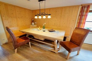 Ein Essbereich mit Holztisch, zwei braunen Stühlen, einer Hängeleuchte und einem Fenster mit Vorhängen.