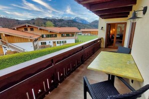 Ein Balkon mit Tisch und Stühlen, ein Holzzaun und Blick auf Häuser und Berge.