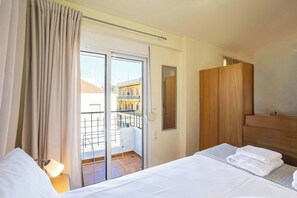 A hotel room with a bed, a wooden wardrobe, a mirror, and a sliding glass door leading to a balcony. - Modern City-Center Studio in the Heart of Kalamata (Kalamata)