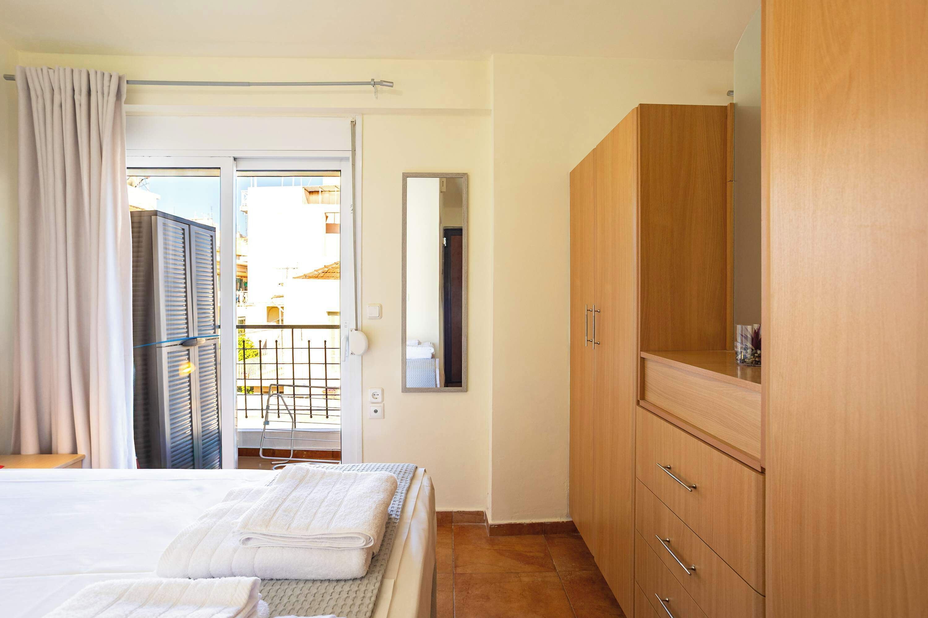 Quarto com cama, guarda-roupa de madeira, porta de banheiro e vista por uma porta de vidro.