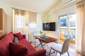 A furnished room with a sofa, a table, a chair, a TV, and a balcony with outdoor furniture. - Modern City-Center Studio in the Heart of Kalamata (Kalamata)