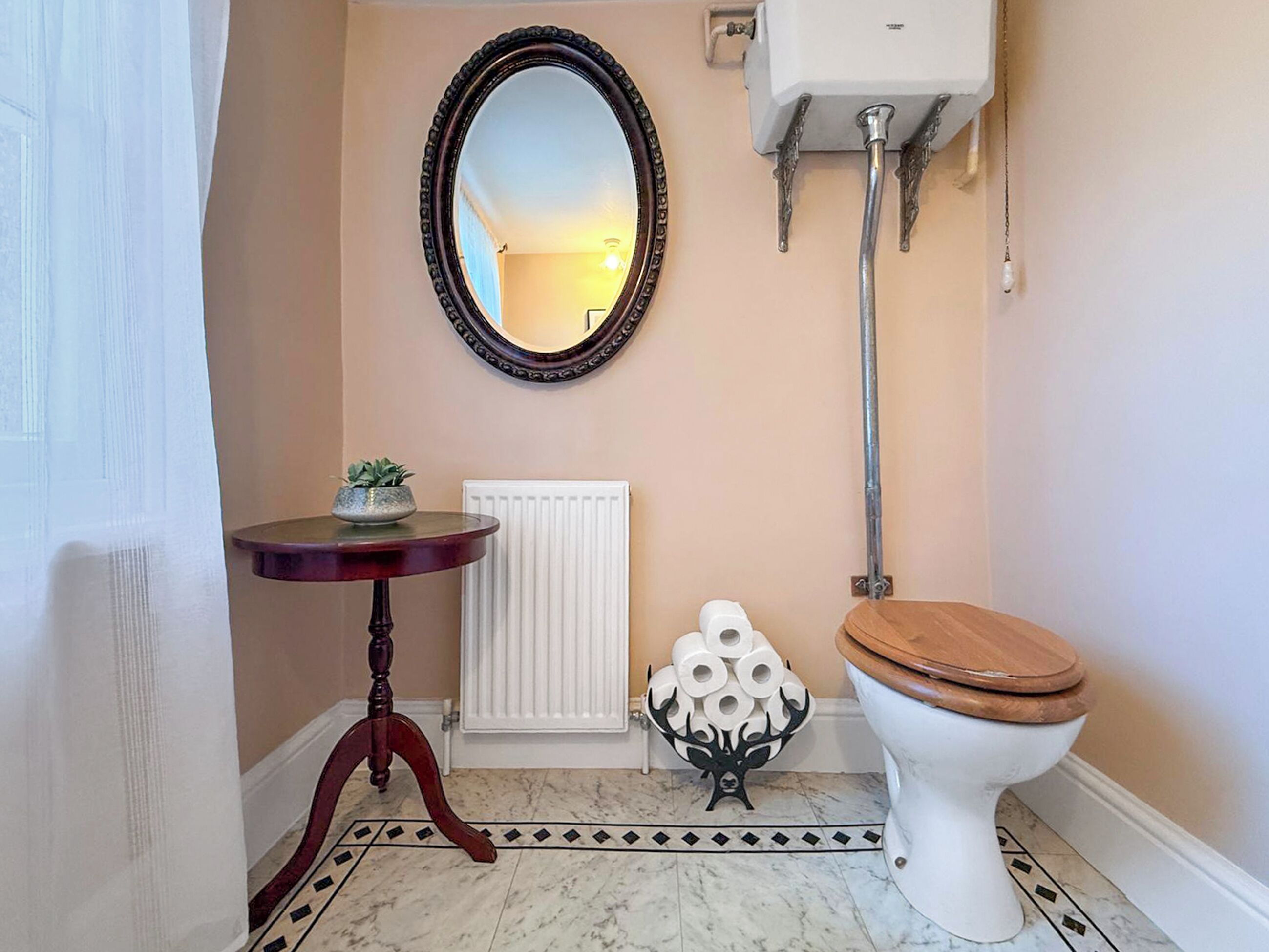 A bathroom with a toilet, a radiator, a mirror, and a small table with a plant.
