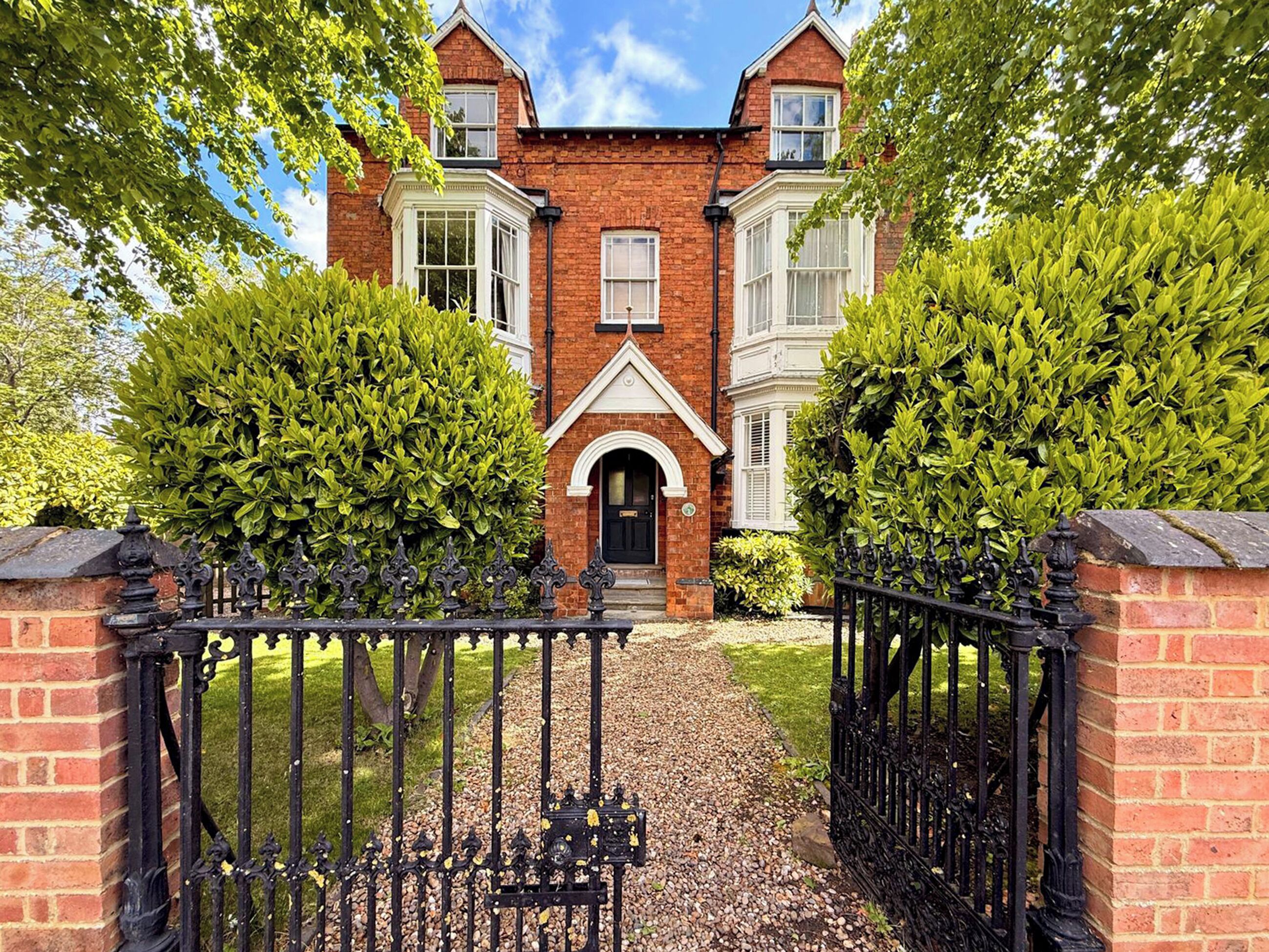 Une maison en briques avec un portail noir, une porte d’entrée et une allée menant à l’entrée.