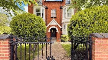 Une maison en briques avec un portail noir, une porte d’entrée et une allée menant à l’entrée.