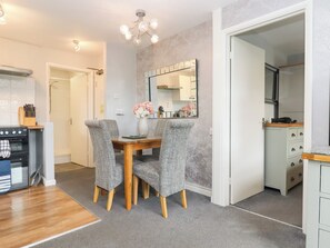 A dining area with a wooden table and grey upholstered chairs, a kitchen with a stove and cabinets, and a mirror on the wall. - Apartment 10 (Torquay)