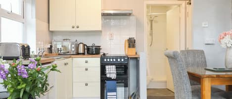 A compact kitchen with a stove, oven, and toaster, a dining area with a table and chairs, and a shower area.