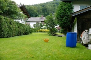 Ein grünes Rasenstück mit einem gelben Gießkann, einem blauen Fass und einem Haus mit geneigtem Dach.