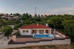 Ein modernes Haus mit Swimmingpool, umgeben von viel Grün und blauem Himmel.