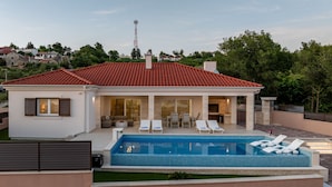Une maison moderne dotée d’une piscine, de chaises longues et d’un espace patio.