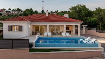 Una casa moderna con piscina, sillas de descanso y una zona de patio.