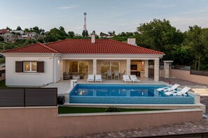 Ein modernes Haus mit Swimmingpool, Liegestühlen und einer Terrassenfläche.