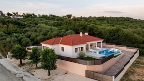 Une maison moderne avec une piscine, entourée d’arbres et de collines.