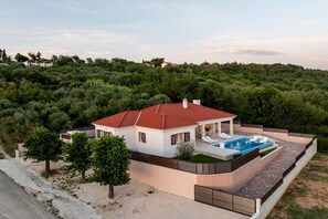 Ein modernes Haus mit Swimmingpool, umgeben von Bäumen und Hügeln.