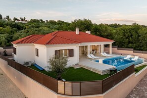 Ein modernes Haus mit Swimmingpool, überdachter Terrasse und umzäunter Garten.