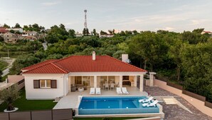 Une maison moderne dotée d’une piscine, d’un espace salon extérieur et offrant une vue sur la verdure environnante.