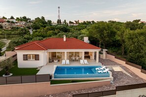 Ein modernes Haus mit Swimmingpool, Sitzgelegenheiten im Freien und Blick auf die umliegende Natur.