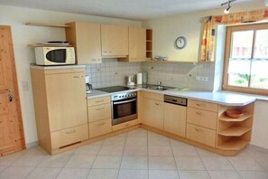 A compact kitchen with wooden cabinets, a microwave, a stove, a sink, and a window with curtains. - Apartment in Rückholz with swimming pool (Rückholz)
