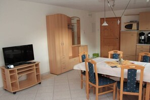 A room with a TV on a stand, a dining table with chairs, wooden cabinets, and a microwave. - Apartment in Rückholz with swimming pool (Rückholz)