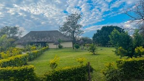 A rural setting with a thatched-roof building, a well-maintained lawn, and a clear sky. - Xisakeni Lodge and Transfers  (Thulamahashe)
