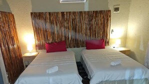 A hotel room with two beds, a wooden headboard, a small window, and a nightstand with a lamp. - Xisakeni Lodge and Transfers  (Thulamahashe)