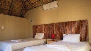 Two single beds with white linens, a red lamp on a nightstand, and a thatched roof ceiling. - Xisakeni Lodge and Transfers  (Thulamahashe)
