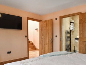 A bedroom with a bed, wooden wardrobe, a TV mounted on the wall, a bathroom with a towel rack, and a staircase leading to another room. - Pabi - Poppy - UKC7077 (Nansidyll)
