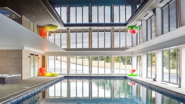 Una piscina interior amb parets de vidre transparent, un paviment de rajola i vista exterior.