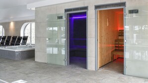 Zona d'una piscina interior moderna amb un bany d'hidromassatge tancat per vidre, una sauna de fusta i un paviment de rajola.