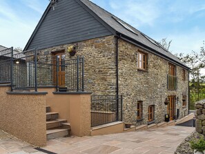 A stone building with a dark roof, a balcony with metal railings, and a set of stairs leading to the entrance. - Pabi - Poppy - UKC7077 (Nansidyll)